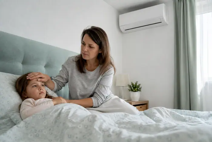 Mama verifica fruntea copilului langa aerul conditionat